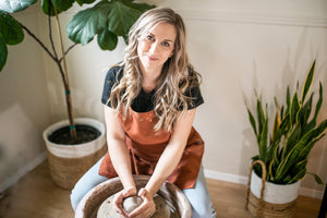 potter in studio sitting at the pottery wheel with a ball of clay and snake plant